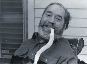 A photo of Ed Roberts, seated and using his ventilator.